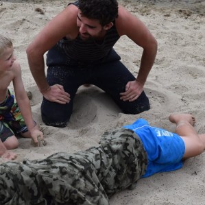 An instructor kneels beside children on the beach showing them how help an unconscious person rescued from the water.