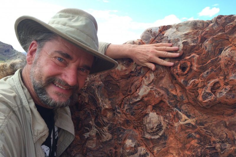Dr. Bruce Damer stands next to a 3.6-billion-year-old artifact representing buried layers of molecular structures, thought to be the framework for the origin of life.