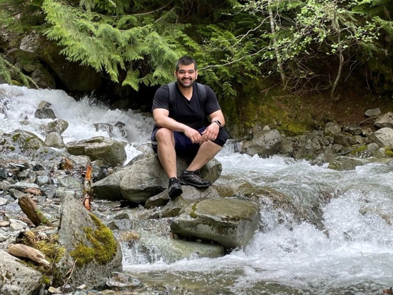 A man sitting on a rock in the middle of a rushing creek.