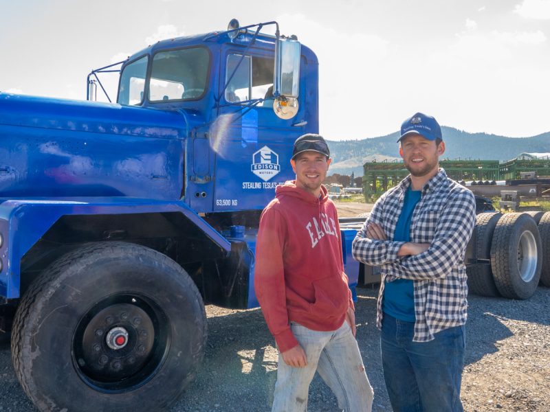 Two men stand in front of a semi-truck