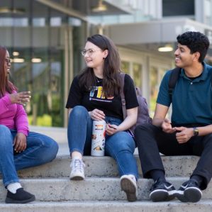 Three university students sitting on the steps outside talking.