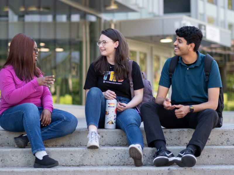 Three university students sitting on the steps outside talking.