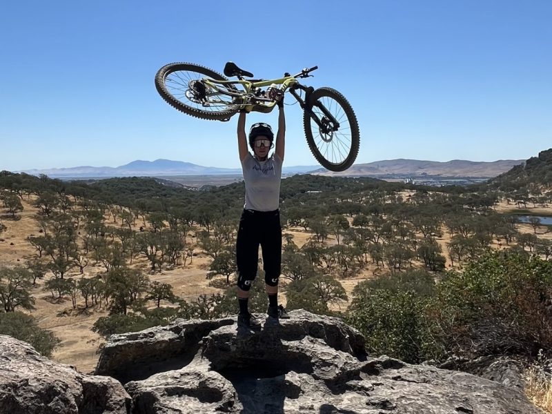 Woman holding a mountain bike in the air a top a large rock.