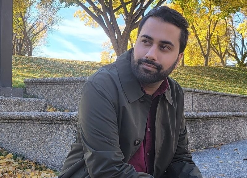 TRU alum Shaminder Parmar sitting on a park bench.