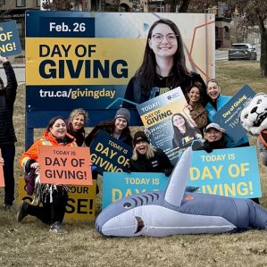 A group of excited people with signs about TRU Day of Giving