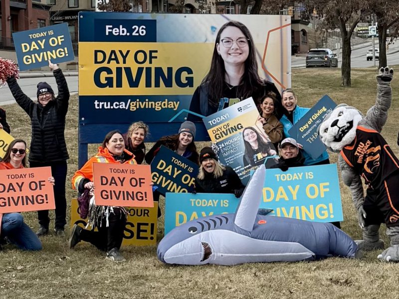 A group of excited people with signs about TRU Day of Giving