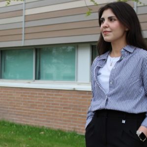 A female business student stands outside a university building looking into the distance.