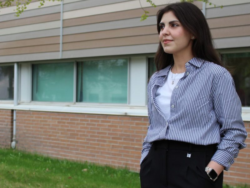 A female business student stands outside a university building looking into the distance.